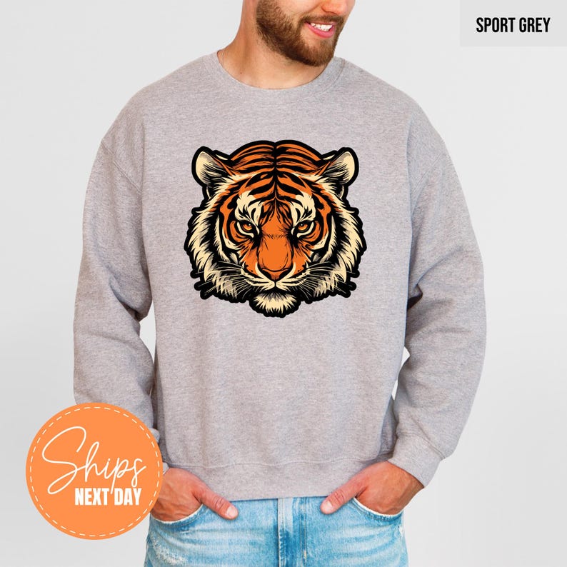 A man wearing a grey sweatshirt with a graphic of a tiger's head printed on it.