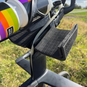 May include: Black bicycle handlebars with a water bottle holder and a water bottle. The water bottle has a rainbow design and the text "NOURISH EDITION". The handlebars have the text "ERGON" and "NORD".