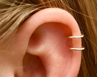May include: A close-up of a person's ear with two gold hoop earrings. The earrings are worn in the upper cartilage of the ear.