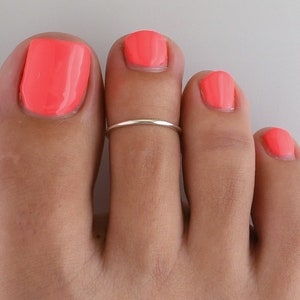 May include: A silver toe ring on a foot with coral pink nail polish.