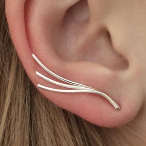 May include: Silver ear cuff with three curved lines. The ear cuff is worn on the upper part of the ear.