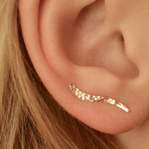 May include: A gold ear cuff with a hammered texture. The cuff is curved and has a pointed end.