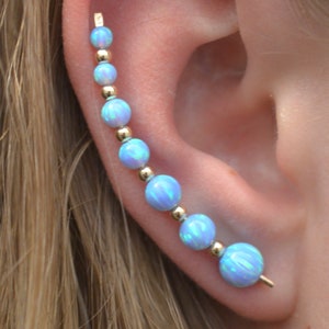 May include: A gold ear cuff with a row of iridescent blue opal beads. The cuff is curved to fit the shape of the ear.