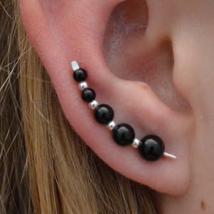 May include: A silver ear cuff with black beads. The cuff is curved and has a small silver post at the end.