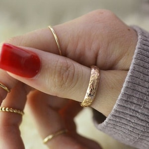 May include: A hand with red nail polish is wearing several gold rings, including a textured band ring.
