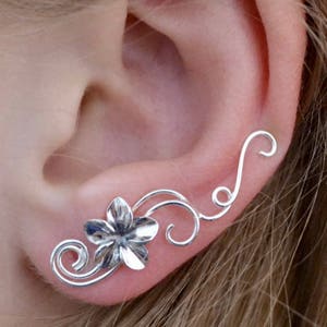 May include: Silver ear cuff with a delicate floral design. The cuff features a small flower with a swirl pattern and a long, curved stem that wraps around the ear.