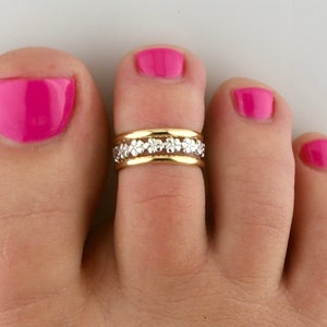 Könnte beinhalten: Goldener Zehenring mit einem Band aus kleinen weißen Blüten.