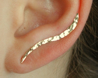 May include: A gold ear cuff with a hammered finish. The cuff is curved and has a subtle shine.