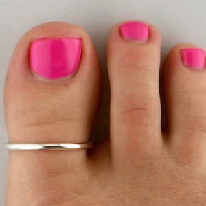May include: A silver toe ring on a foot with pink nail polish.