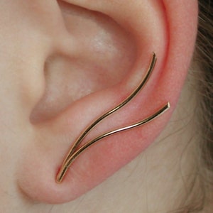 May include: A pair of gold ear cuffs, one curved and the other straight, are worn on the upper part of the ear.