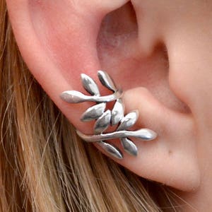 May include: Silver ear cuff with a leaf design. The cuff is worn on the upper part of the ear.