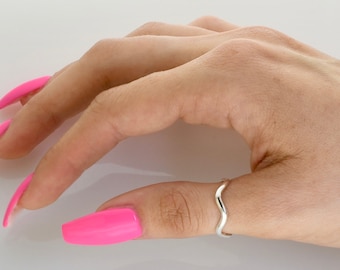 May include: A silver wavy ring worn on a finger with bright pink nail polish.