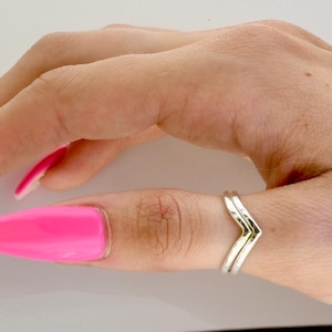 Könnte beinhalten: Zwei silberne Chevron-Ringe, die an einem Finger getragen werden. Die Ringe sind übereinander gestapelt.