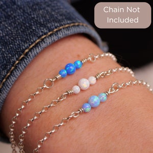 May include: Three silver chain bracelets with opal beads. The top bracelet has three blue opal beads, the middle bracelet has three white opal beads, and the bottom bracelet has three blue opal beads. The text "Chain Not Included" is visible in the image.