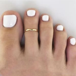 May include: A close-up of a foot with white nail polish on each toe. A gold toe ring is worn on the second toe.