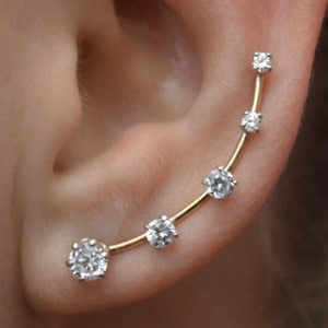 May include: A gold ear cuff with five clear cubic zirconia stones set along the curved bar. The ear cuff is designed to be worn on the upper ear.