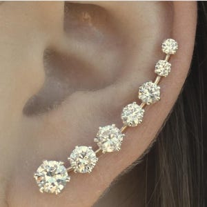 May include: A gold ear cuff with a row of clear sparkling rhinestones. The ear cuff is curved and has a delicate design.