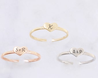 Könnte beinhalten: Drei verstellbare herzförmige Ringe in Gold, Roségold und Silber. Jeder Ring hat einen herzförmigen Anhänger mit eingravierten Initialen. Der goldene Ring hat den Buchstaben "K", der roségoldene Ring "S+R" und der silberne Ring "A&P".