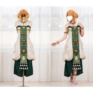 Op de afbeelding: Een kostuum bestaande uit een cr&egrave;mekleurig strapless lijfje en een donkergroene rok. Een lange, groene tabard in het midden is versierd met goudkleurige geometrische metalen accenten en bungelende witte driehoekige bedels. Inclusief blonde pruik.