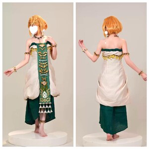 Op de afbeelding: Een kostuum bestaande uit een cr&egrave;mekleurig strapless lijfje met een donkergroen stoffen paneel aan de voorzijde, versierd met gouden geometrische accenten en hangende driehoekige bedels. De outfit bevat een donkergroene rok, gouden armbanden en een ketting.