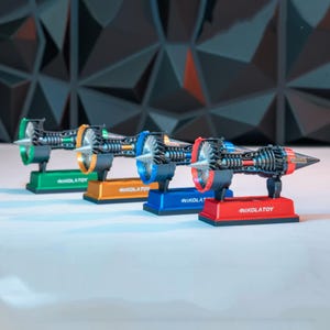 May include: Four miniature jet engine models in green, orange, blue, and red. Each model has a detailed internal structure and is mounted on a matching base with the text "NIKOLATOY". The engines are displayed against a dark geometric background.