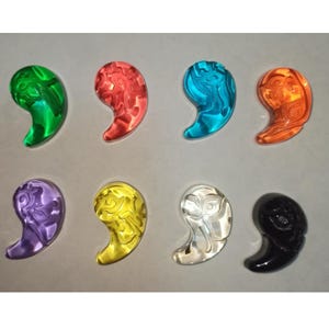 Pode incluir: Um conjunto de oito pingentes em forma de vírgula dispostos em duas filas. Os pingentes são translúcidos em verde, vermelho, azul, laranja, roxo, amarelo e transparente, com uma peça preta sólida. Cada um apresenta um padrão em relevo.