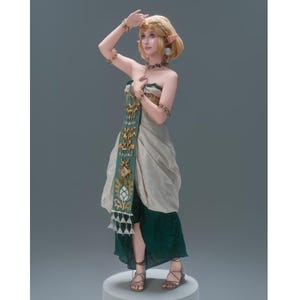 Op de afbeelding: Een blond elfenfiguur met puntige oren draagt een strapless, gelaagde outfit in beige en donkergroen. Het kledingstuk heeft een lang, verticaal groen paneel versierd met gouden geometrische patronen en bungelende driehoekige bedels.