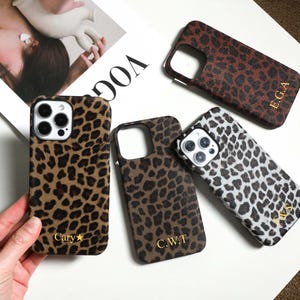 Puede incluir: Cuatro fundas rectangulares para teléfono con estampado de leopardo. Tres fundas presentan iniciales o nombres monogramados en color dorado, incluyendo E.G.A, C.W.T y Cary con una estrella. Las fundas tienen recortes para las lentes de la cámara.