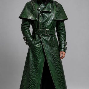 May include: A long, emerald green trench coat featuring a textured snakeskin pattern, a high collar, a wide shoulder cape, and a belted waist. The coat includes silver-toned metal buckles on the shoulders and cuffs, with a button-down front closure.