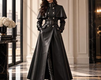 May include: A floor-length black leather coat featuring a high collar with a buckle, a double-breasted front with silver buttons, a matching waist belt, and a cape-style overlay on the shoulders. The coat has long sleeves and a flared skirt.