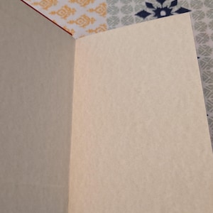 Pu&ograve; includere: Quaderno aperto con pagine color crema e copertina rossa. Le pagine sono bianche, pronte per scrivere o disegnare. Il quaderno &egrave; aperto, rivelando le pagine interne e la rilegatura.