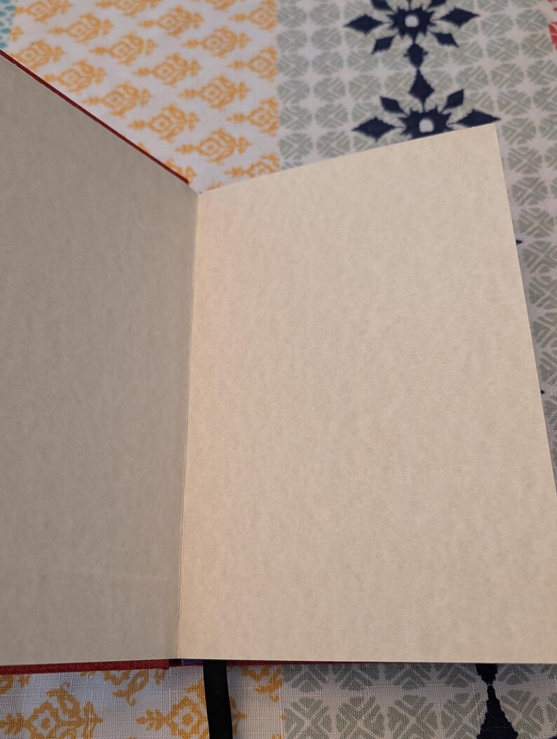 Pu&ograve; includere: Quaderno aperto con pagine color crema e copertina rossa. Le pagine sono bianche, pronte per scrivere o disegnare. Il quaderno &egrave; aperto, rivelando le pagine interne e la rilegatura.