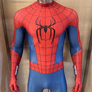 May include: A full-body red and blue textured spandex suit featuring a black spider emblem on the chest, a black web pattern across the red sections, and silver mechanical wrist attachments on each arm, displayed on a metallic mannequin torso.