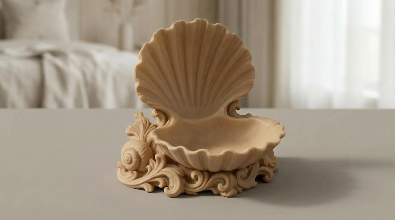 Puede incluir: Un plato decorativo beige con forma de concha. El plato presenta un dise&ntilde;o de concha grande y abierta con una superficie detallada y texturizada. La base est&aacute; adornada con volutas ornamentadas y un acento de concha, creando un tema costero.