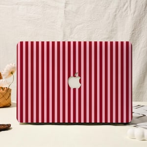 Puede incluir: Funda para portátil con un diseño de rayas verticales en tonos rojos y rosas. El logotipo de Apple es visible en el centro. Diseñada para un portátil.
