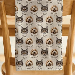 May include: A rectangular kitchen towel with a repeating pattern of cat and dog faces. The cat faces are labeled with the name Oliver, and the dog faces are labeled with the name Winston. The towel has a light beige background with a subtle grid texture.