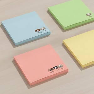 May include: Four square sticky note pads in pastel colors: blue, green, pink, and yellow. Each pad features a pet illustration and a name. The blue pad has two dogs and the text "Bailey, Max". The green pad has a dog and the name "Cody". The pink pad has three dogs and the text "Ralph, Max, Cooper". The yellow pad has a cat and the name "Cody".