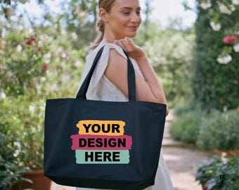 May include: A navy blue tote bag with the text "YOUR DESIGN HERE" in yellow, pink, and teal. The bag has black handles and is being carried outdoors. The bag is a large size, suitable for carrying groceries or other items.