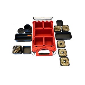May include: A red, compartmentalized storage case with a handle, surrounded by black containers and trays. The case has multiple compartments and is designed for organizing small items. Several containers are filled with small, gold-colored objects.