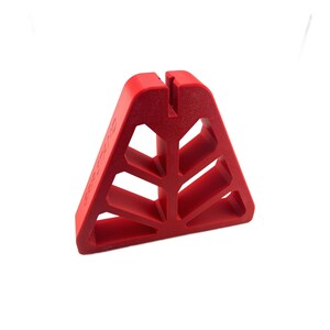 May include: A red, triangular Grip Stand with a textured surface. The stand has a slot at the top and cut-out geometric shapes. The words "GRIP STAND" are printed on the side.
