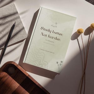 Könnte beinhalten: Ein hellgrünes Notizbuch mit dem aufgedruckten Text Study better: Not harder. auf dem Einband. Der Einband zeigt eine kleine Strichzeichnung eines offenen Buches, eines Schmetterlings und wellenförmiger Linien. Ein schwarzer Stift liegt auf einem grauen Block.