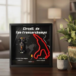 May include: Framed artwork featuring the Circuit de Spa-Francorchamps race track. The black background highlights a red track outline, a miniature race car, and text including "Spa, Belgium" and "6.76 mi". A Belgian flag is also included.