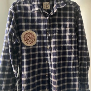 May include: Navy blue and white plaid flannel shirt with a button-down front. The shirt features a circular patch with the text "WIDESPREAD PANIC". The shirt has a "RED HEAD" brand label.