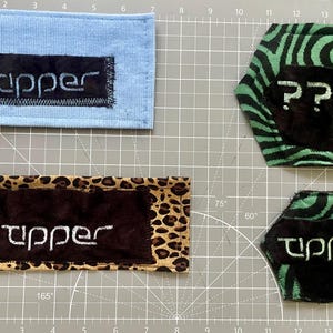 May include: Four fabric patches with embroidered text. One is light blue, one is leopard print, and two are black with green zebra stripes. The word "Tipper" appears on three, and question marks on one.
