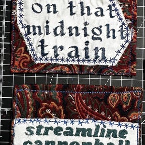 Op de afbeelding: Twee stoffen patches met tekst. De bovenste patch heeft de woorden "Ridin' on that midnight train" in donkerblauwe letters op een witte achtergrond, omlijst door blauwe stiksels. De onderste patch leest "streamline cannonball" in groene letters.