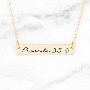Könnte beinhalten: Goldene Bar-Halskette mit der Inschrift "Sprüche 3:5-6" auf weißem Marmor.