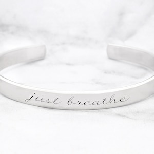 May include: A silver bangle bracelet with the words "just breathe" engraved on the front.