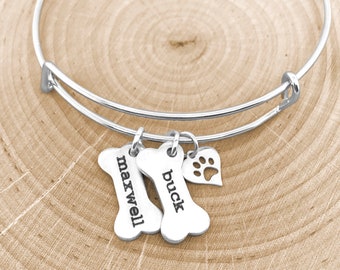 May include: Silver charm bracelet with two bone-shaped charms engraved with the names "Maxwell" and "Buck" and a heart charm with a paw print cutout.