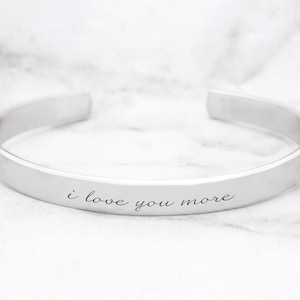 May include: A silver bangle bracelet with the inscription "i love you more" engraved on the front.
