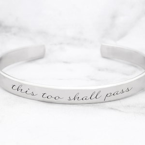 May include: Silver bangle bracelet with the inscription "this too shall pass".